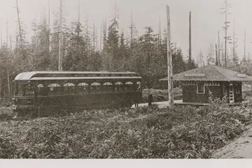 An Interurban car beside a small wooden station, with a cut-over forest of tall stumps behind, in 1910.