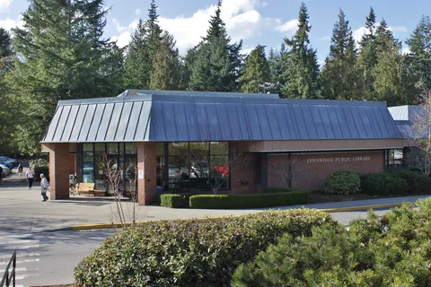 The Lynnwood Library: a low brick building with a pale metal roof, among tall firs.